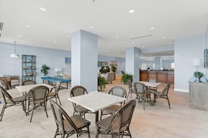 A spacious dining area with high ceilings, modern furniture, and a view of the kitchen in the background.