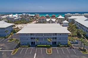 Un hotel de varios pisos con patio central, estacionamiento y vistas a la playa y al océano.