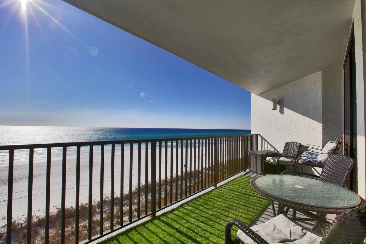 A balcony with a view of the ocean, a glass table, and outdoor seating.