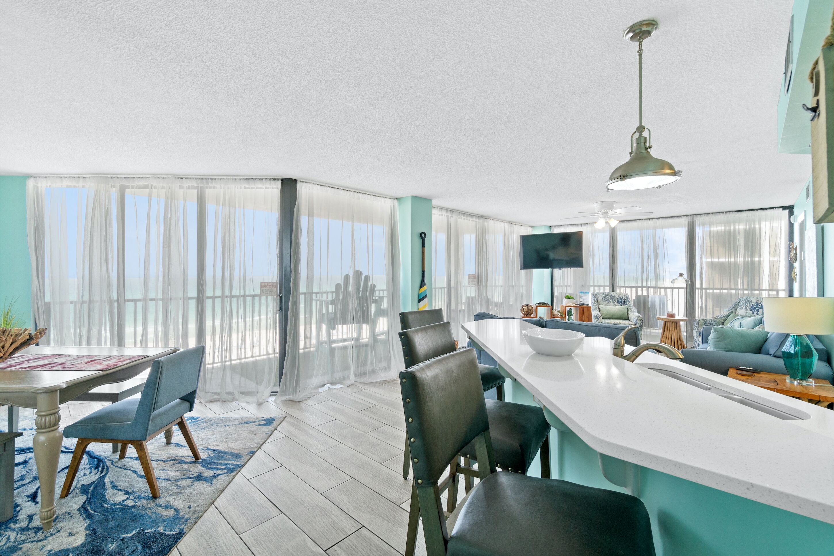 A spacious living area with a large window, a dining table with chairs, a kitchen area with a sink and counter, and a sofa.