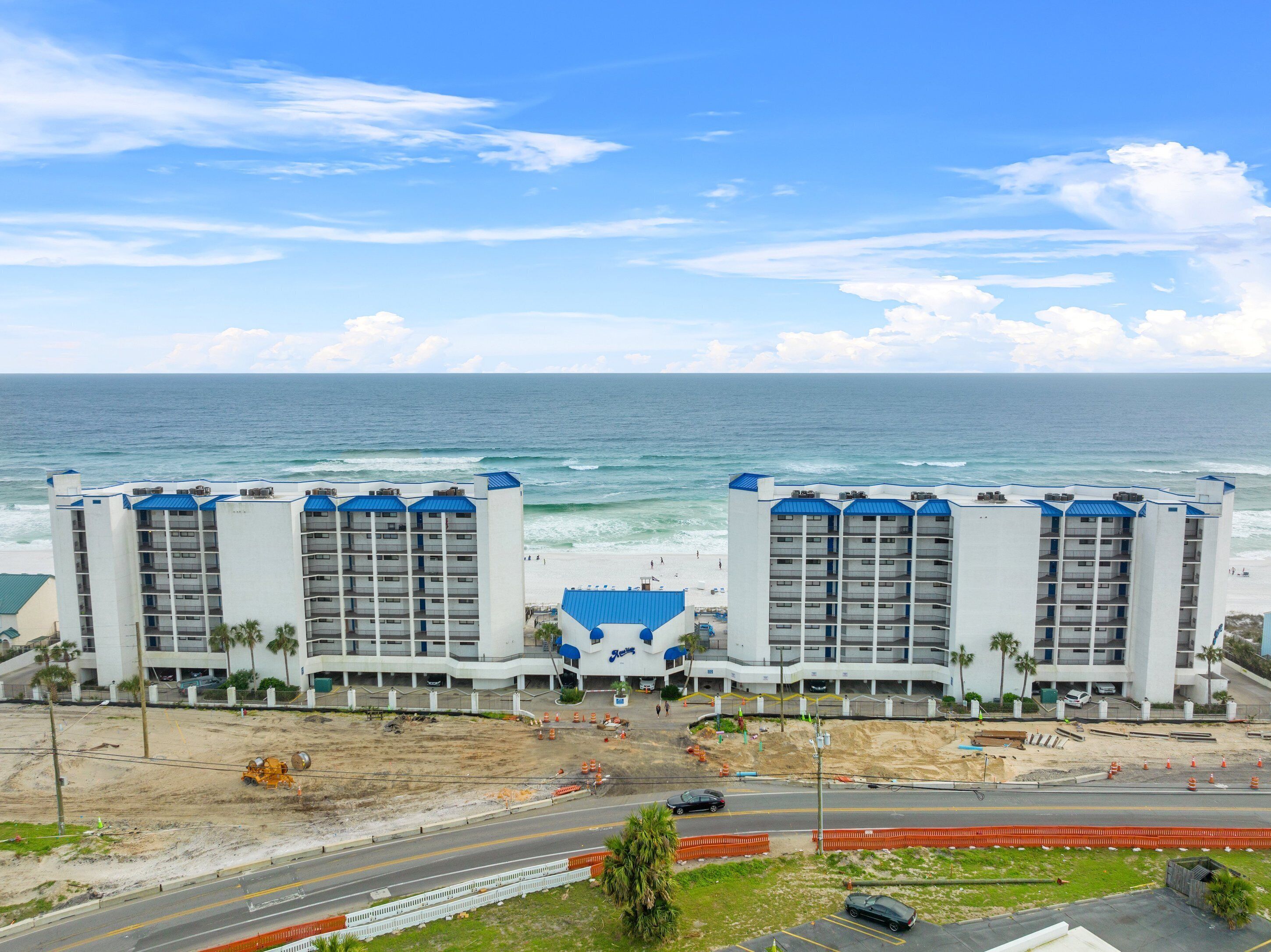 A beachfront hotel with multiple floors and balconies, a sandy beach in front, and the ocean in the background.