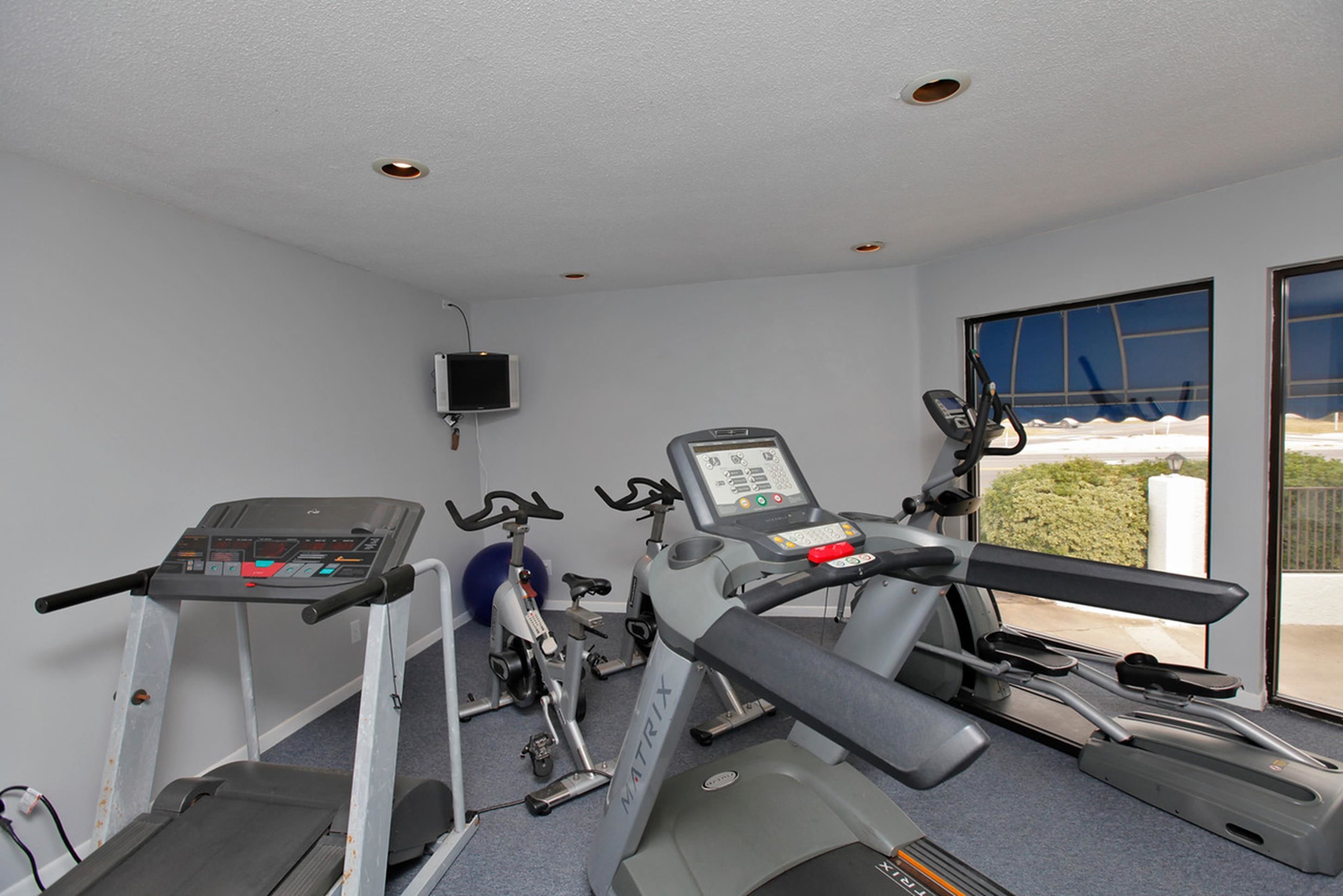 Une salle de sport équipée de tapis de course, de vélos d’appartement et d’un téléviseur fixé au mur.
