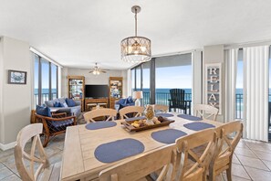 Un comedor amplio con una mesa y sillas de madera, un candelabro y vista al océano.