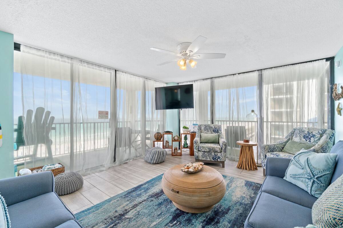 A spacious balcony with a ceiling fan, a flat-screen TV, and a seating area with a sofa and chairs.