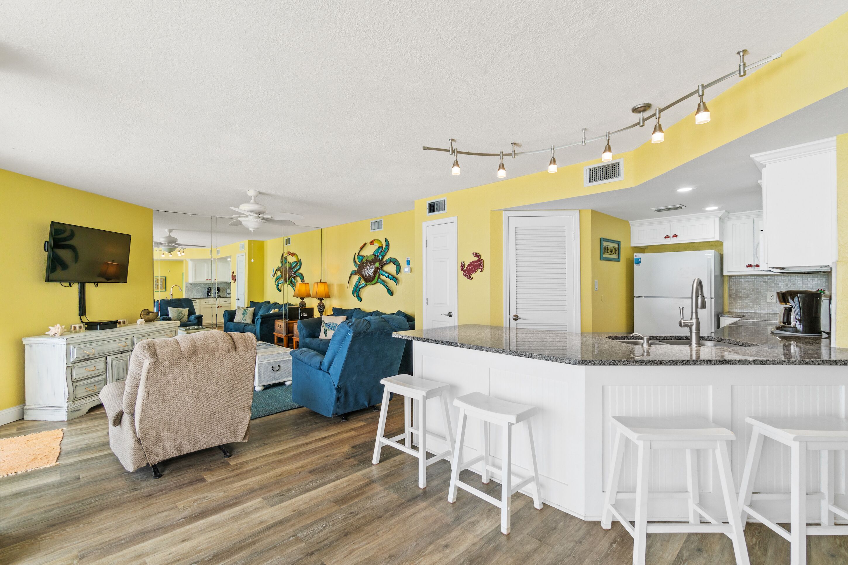 Una cocina moderna con gabinetes blancos, una isla central con taburetes de bar y una pared de acento amarilla.