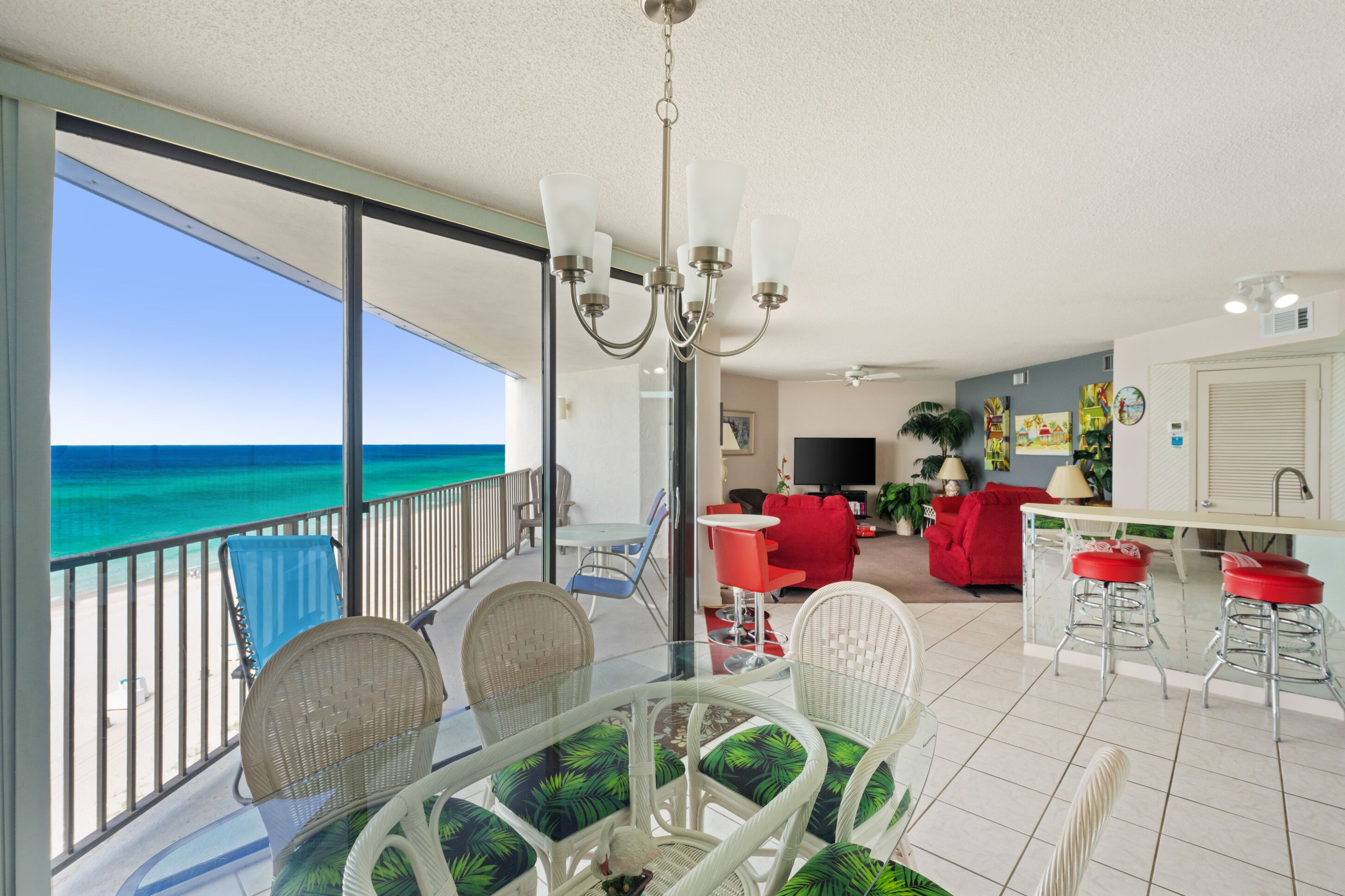A balcony with a glass table and chairs, a red sofa, and a kitchen area with bar stools.