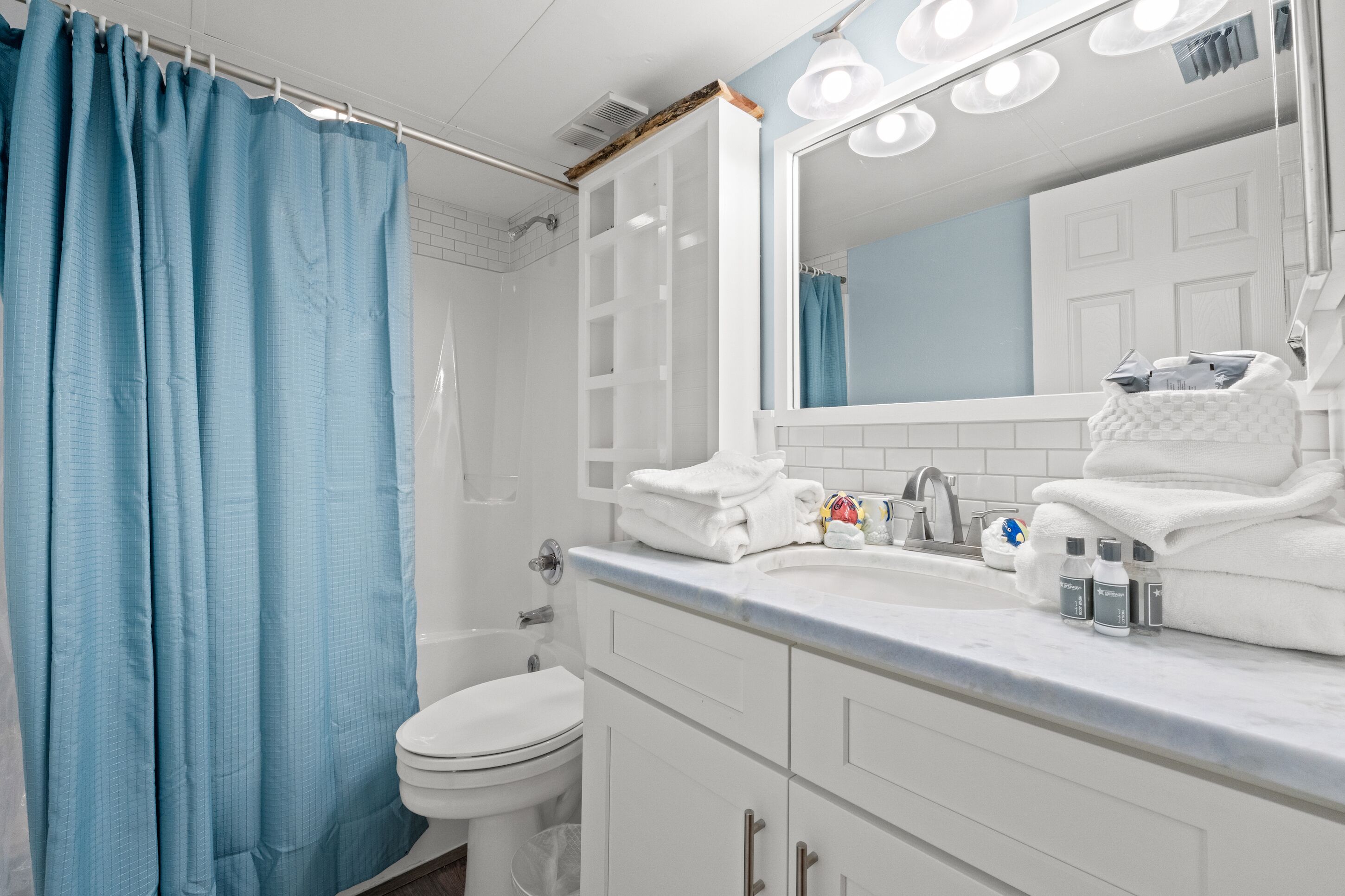 A bathroom with a white sink, mirror, and white cabinets. There is a blue shower curtain and a white toilet.