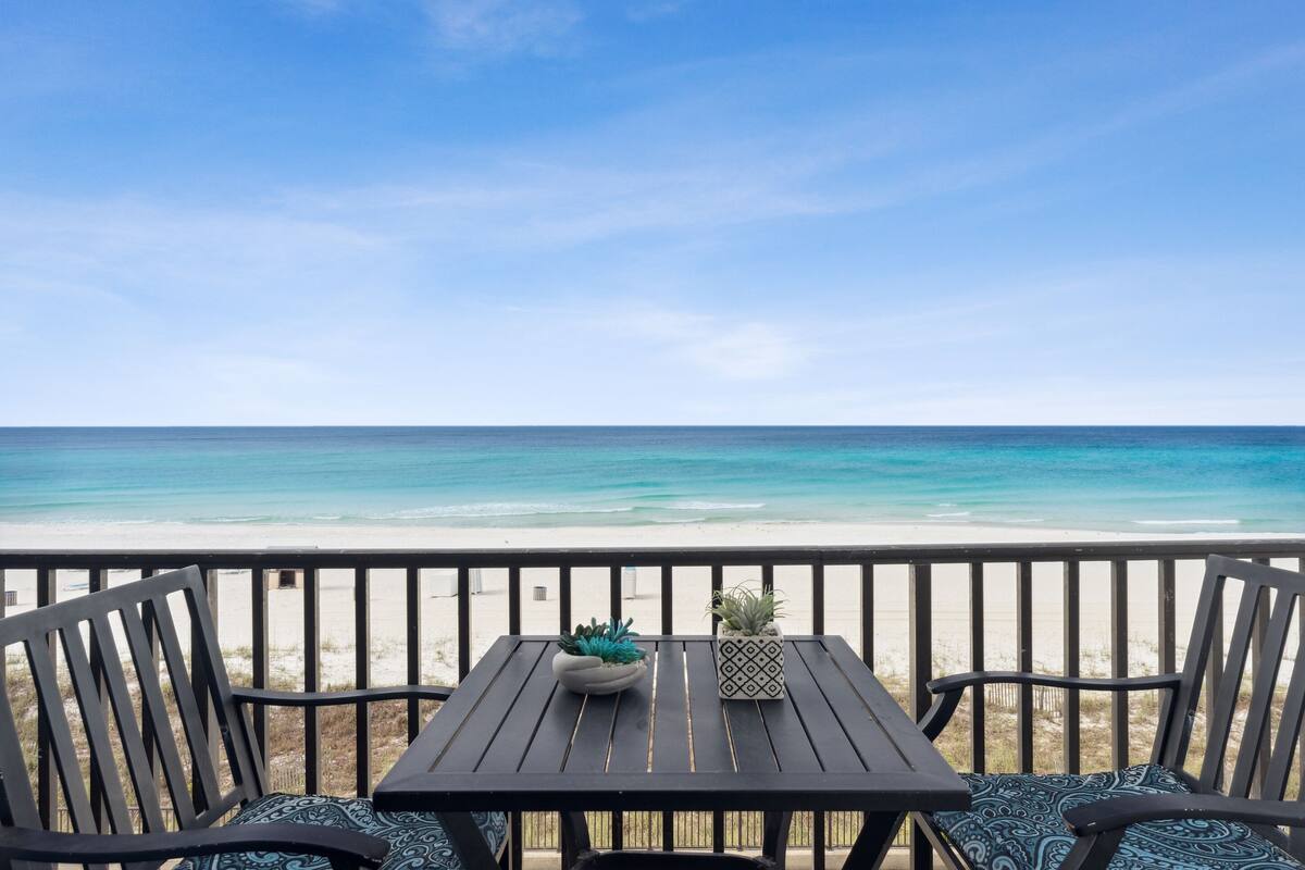 A wooden deck with a table and chairs overlooking a beach.