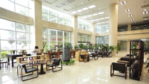 Eine geräumige Lobby mit hohen Decken, großen Fenstern und verschiedenen Sitzgelegenheiten, darunter Tische und Stühle.