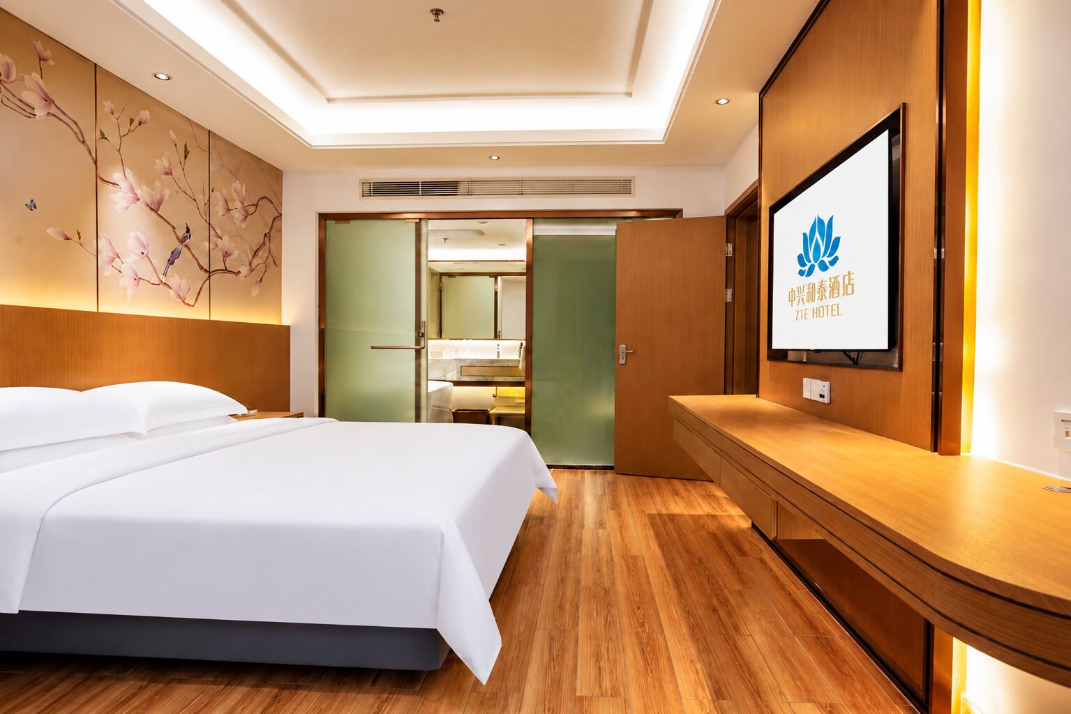 Une chambre d’hôtel comprenant un lit, une commode en bois, un téléviseur fixé au mur et un panneau décoratif mural.