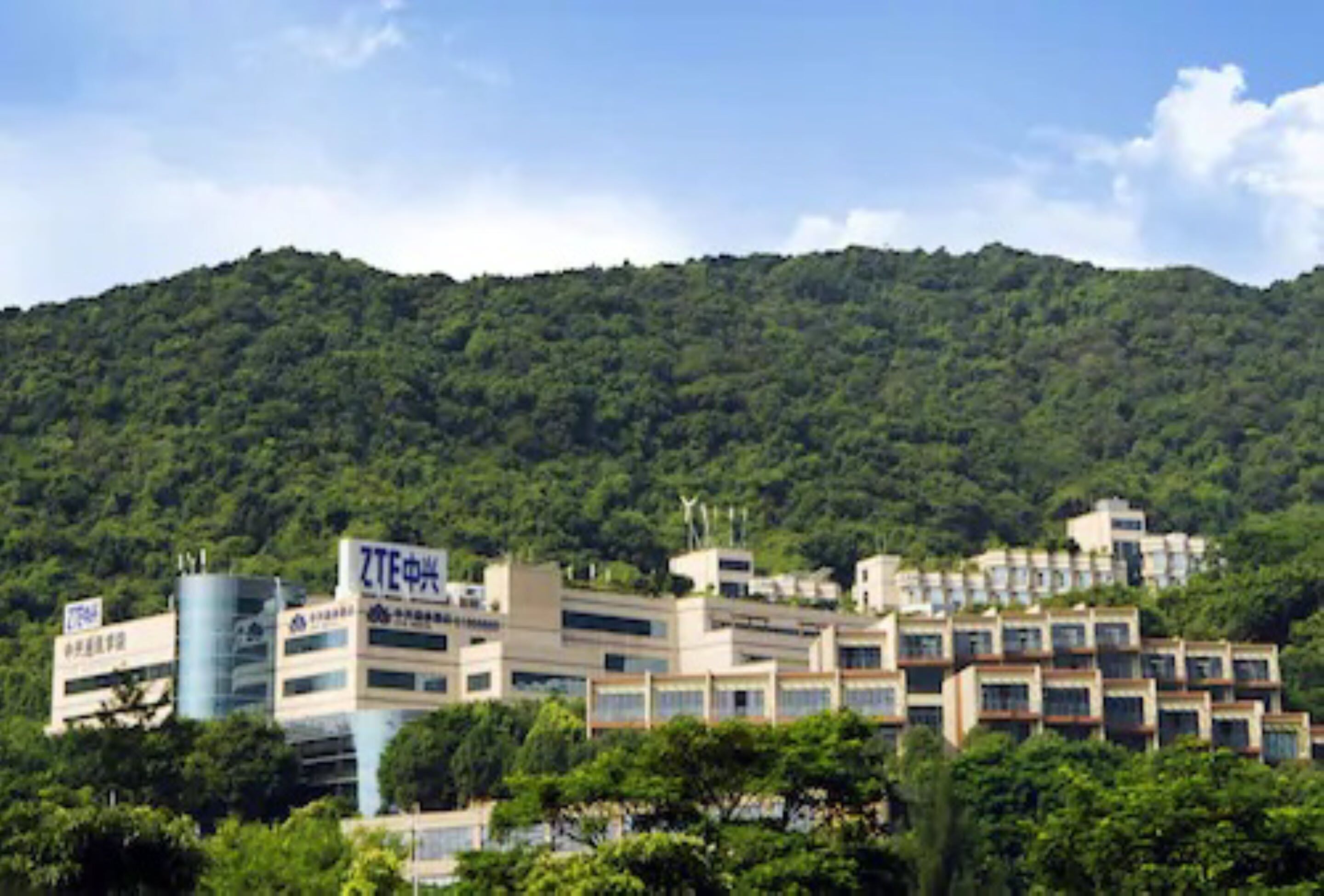 A hotel complex with multiple buildings, surrounded by lush green hills.