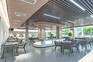 A modern dining area with a central island, seating arrangements, and large windows providing natural light. - ZTE Hotel Da Mei Sha (Shenzhen)