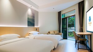 Ein Hotelzimmer mit zwei Betten, einem Schreibtisch und Blick auf Grünflächen.