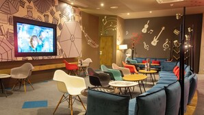 Un espace de détente moderne doté d’un grand téléviseur à écran plat, de sièges aux couleurs vives et d’un mur décoré de notes de musique et d’instruments.