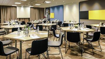 Un salón de conferencias con mesas, sillas, botellas de agua y una pantalla de proyector.