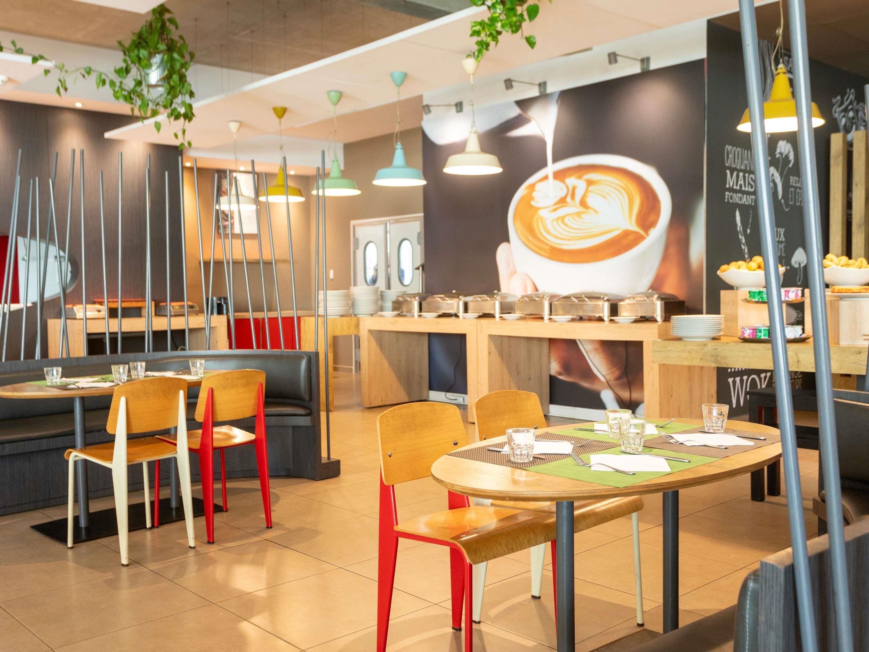 Ein modernes Café-Interieur mit runden Tischen, rot-weißen Stühlen, hängenden Pendelleuchten und einem großflächigen Wandgemälde mit Kaffeemotiven.