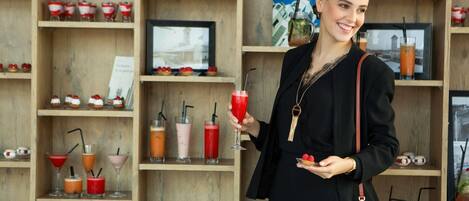 Una persona sosteniendo una bebida con líquido rojo, rodeada de estanterías con varios objetos, incluyendo libros, tazas y cuadros enmarcados.