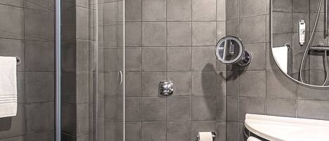 A modern bathroom with a glass shower enclosure, a toilet, a sink with a mirror, and a towel rack.