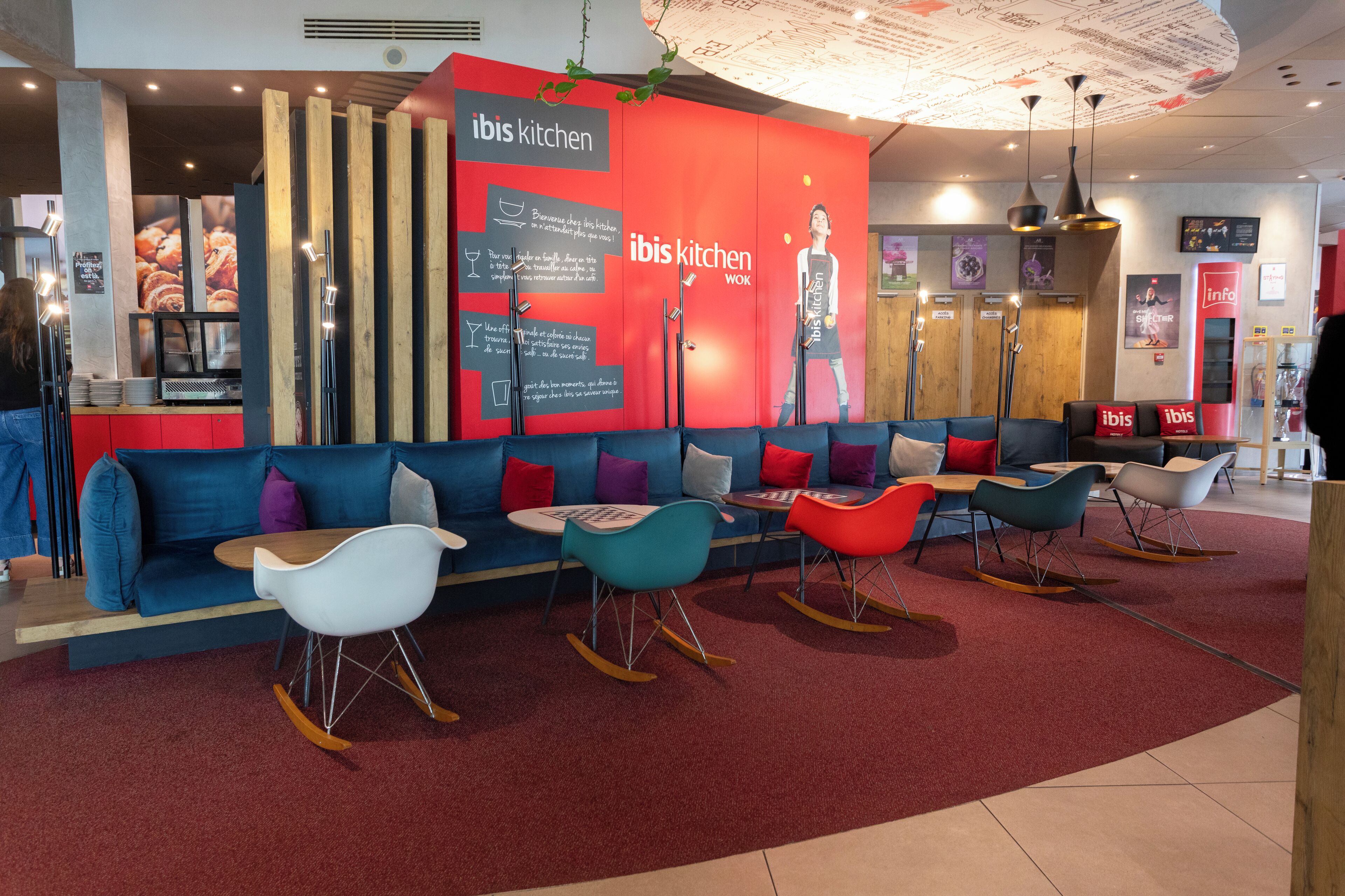 A modern interior with a red and blue color scheme, featuring a sofa, rocking chairs, and a counter with a menu.