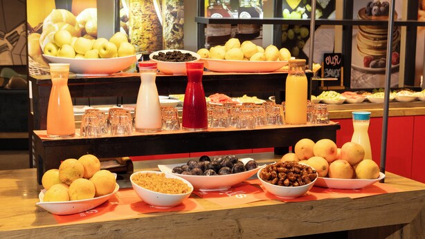 Une table de buffet garnie de divers fruits, de bols remplis de noix et de plusieurs bouteilles de boissons.