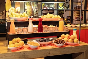 Una mesa de buffet con diversas frutas, tazones de frutos secos y varias botellas de bebidas.