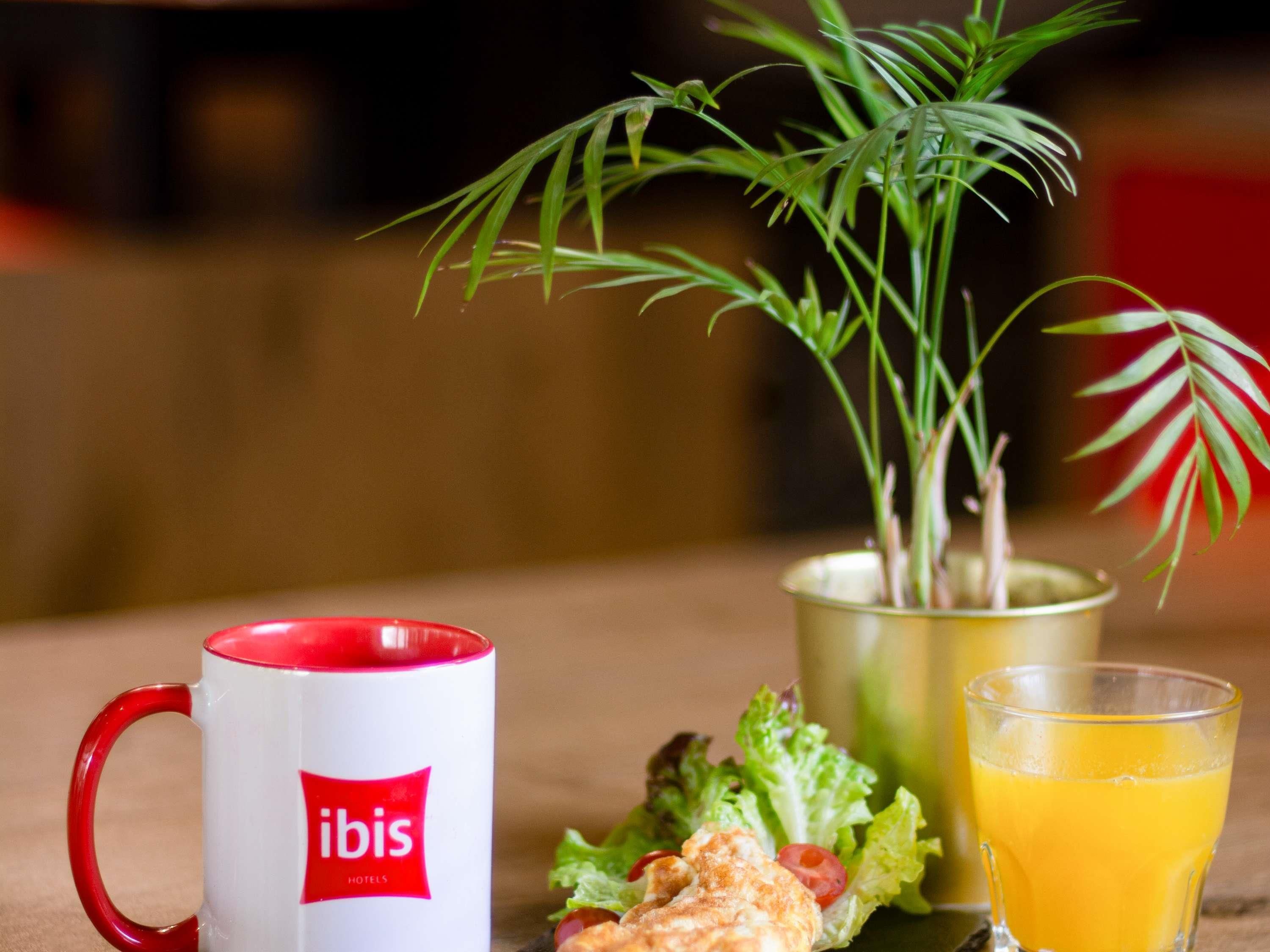 A table with a red and white mug, a glass of orange juice, a small salad, and a potted plant.