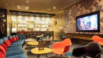A lounge area with a sofa, chairs, tables, a bar, and a TV screen.