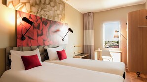 Une chambre d’hôtel avec deux lits, un bureau, une chaise et une grande fenêtre donnant sur un beau paysage.