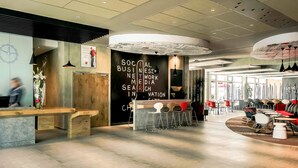 Un espace d’accueil moderne avec un comptoir de réception en bois, un mur noir avec du texte blanc et un coin salon avec des chaises rouges et blanches.