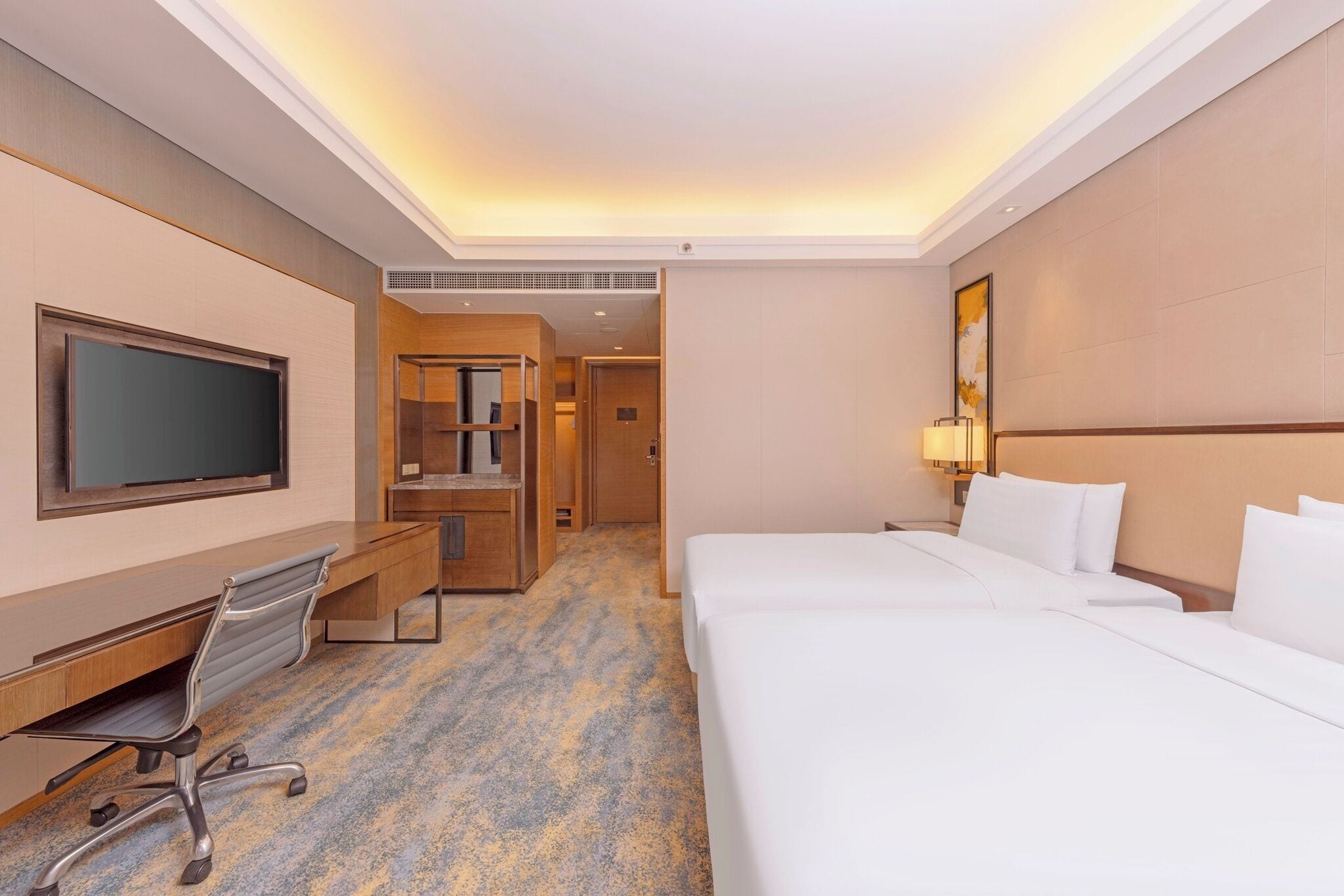 A hotel room with a large bed, a desk with a chair, a television, and a wardrobe.