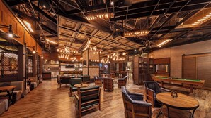 Un grand espace bar avec un plancher en bois, divers types de sièges, notamment des tables et des chaises, et une table de billard.