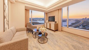 Une chambre d’hôtel moderne dotée d’une grande fenêtre donnant sur la ville, d’un téléviseur à écran plat, d’un canapé et d’une table basse agrémentée d’un vase de fleurs.