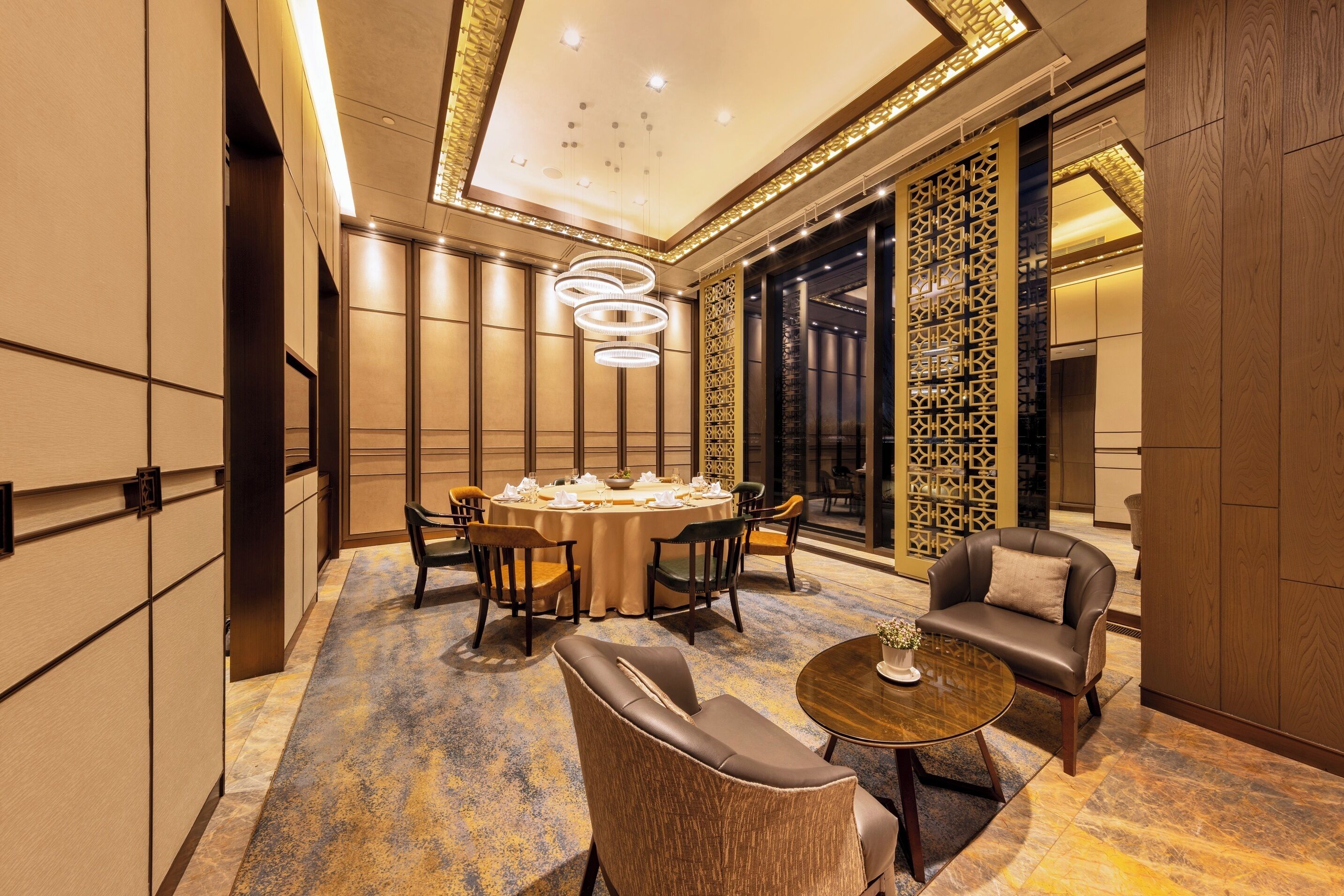 A modern hotel lobby with a round dining table, leather seating, and a decorative wall.