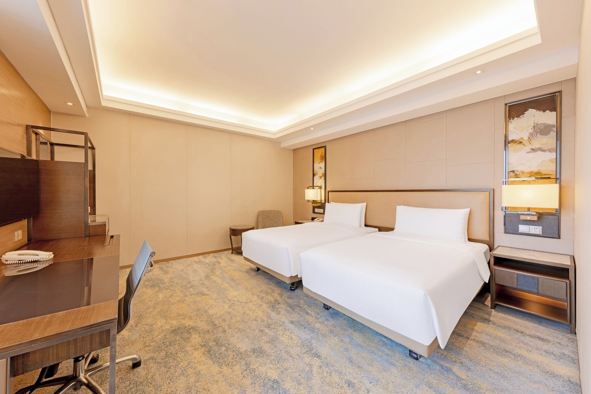 A hotel room with two beds, a desk, a chair, a TV, and a painting on the wall.