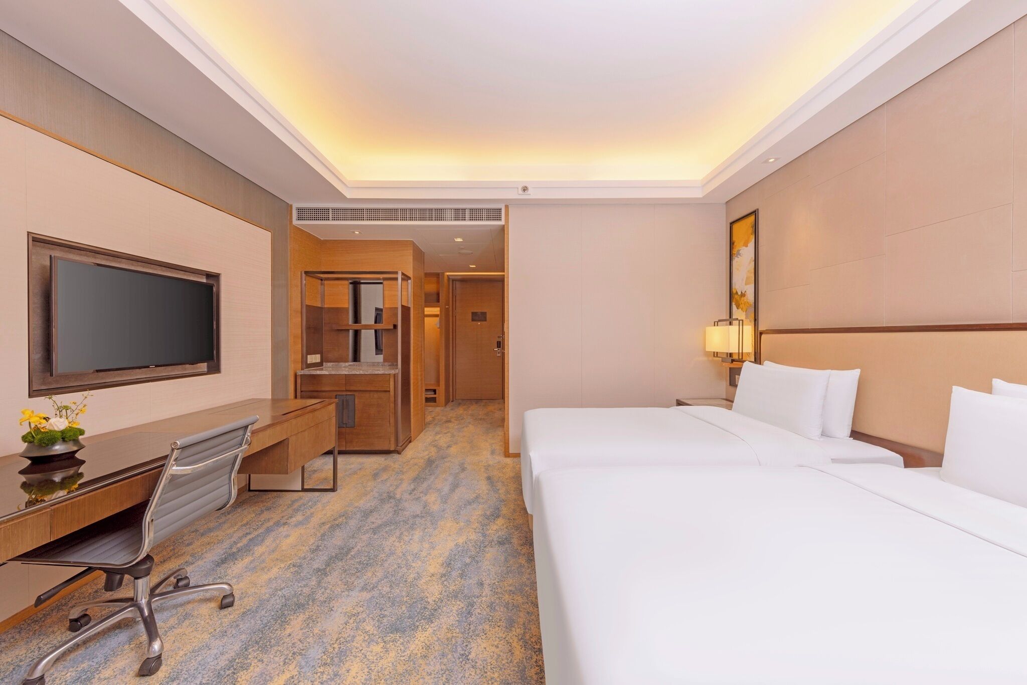 A hotel room with a bed, a desk with a chair, a television, and a bathroom visible through an open door.