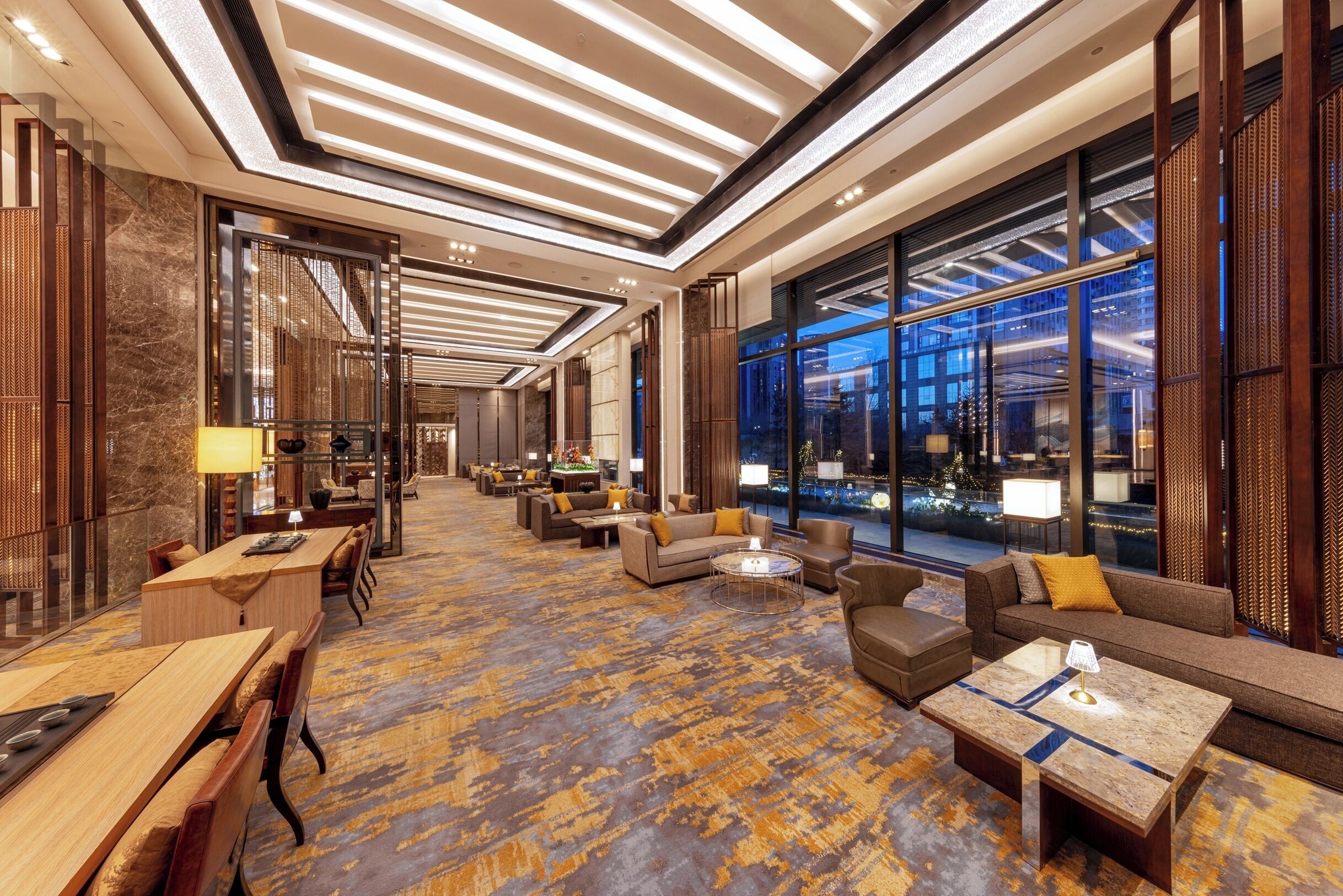 Un vestíbulo espacioso con alfombra estampada, muebles modernos y amplias ventanas que ofrecen vistas panorámicas de la ciudad.