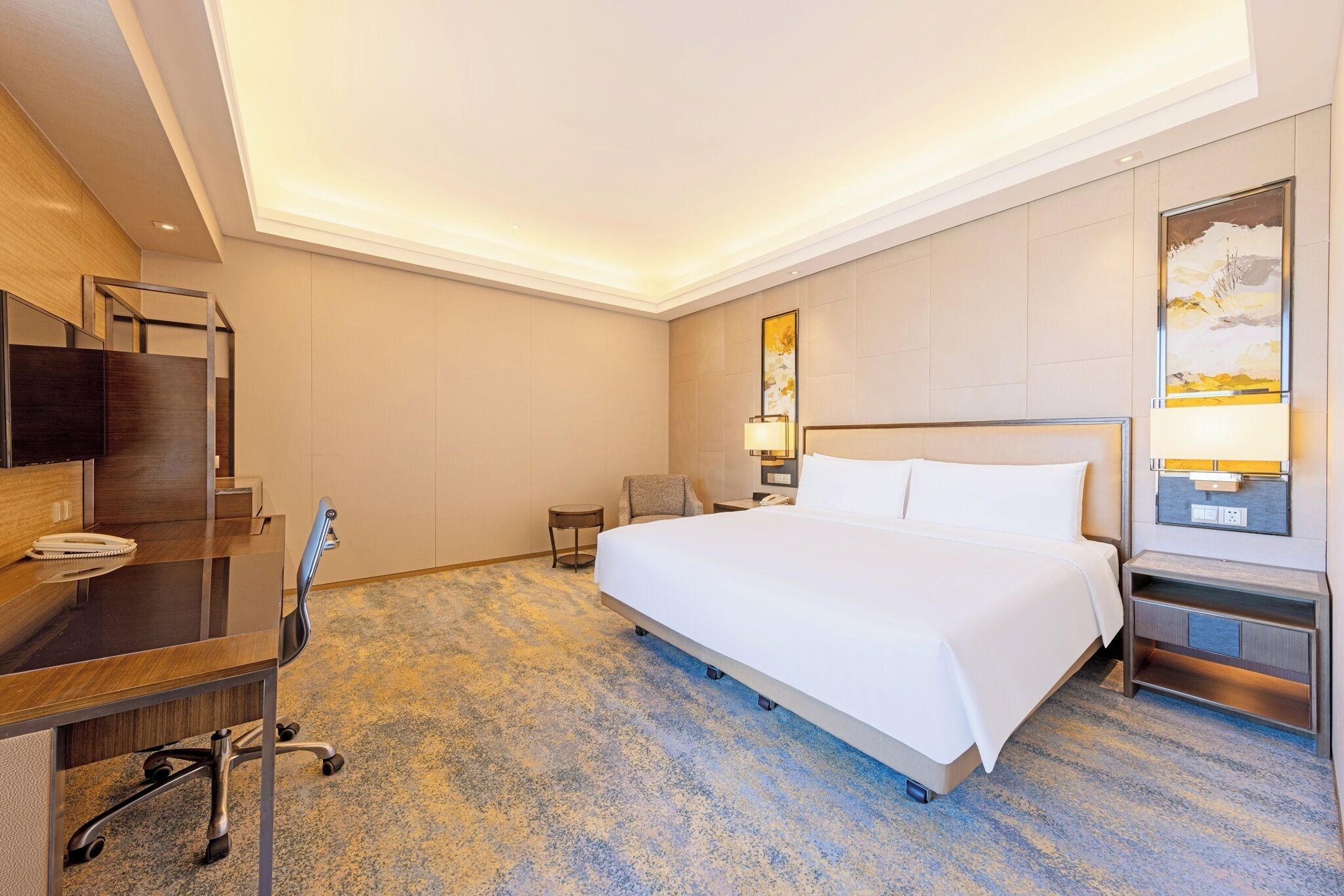 Habitación de hotel con una cama grande, un escritorio con silla, una mesita pequeña y un televisor montado en la pared.