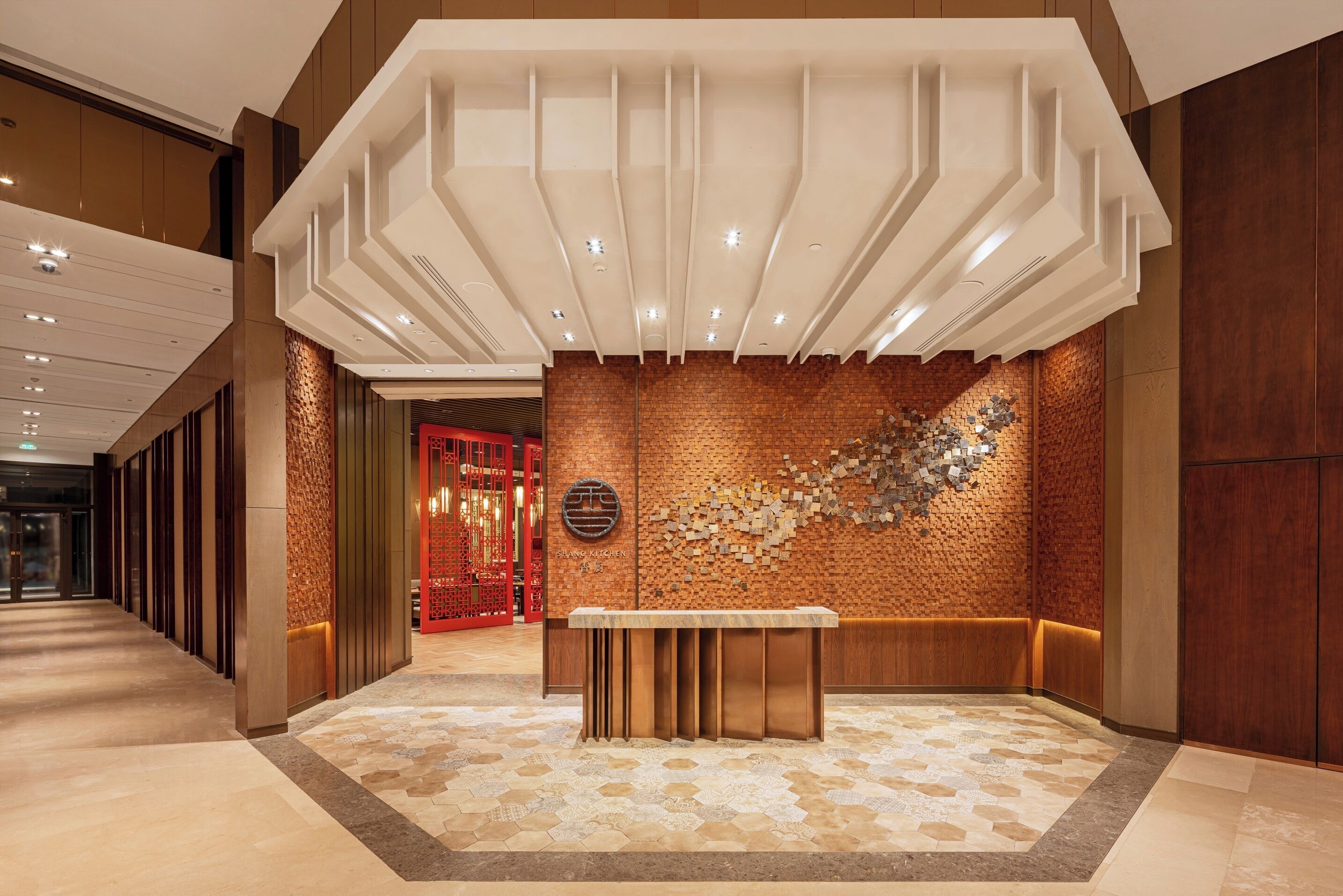 A lobby with a modern design, featuring a reception desk, a patterned wall, and a geometric ceiling structure.
