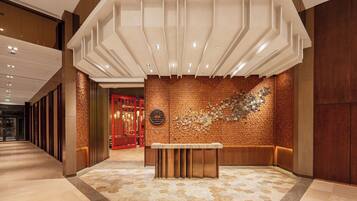 A lobby with a modern design, featuring a reception desk, a patterned wall, and a geometric ceiling structure.