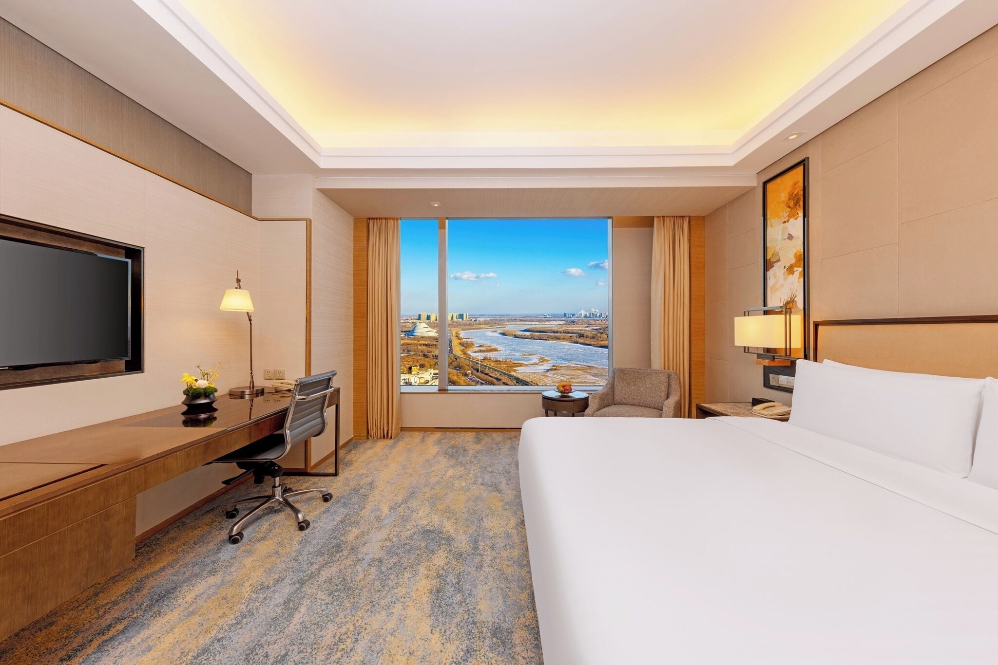A hotel room with a large bed, a desk, a chair, a TV, and a large window offering a city view.