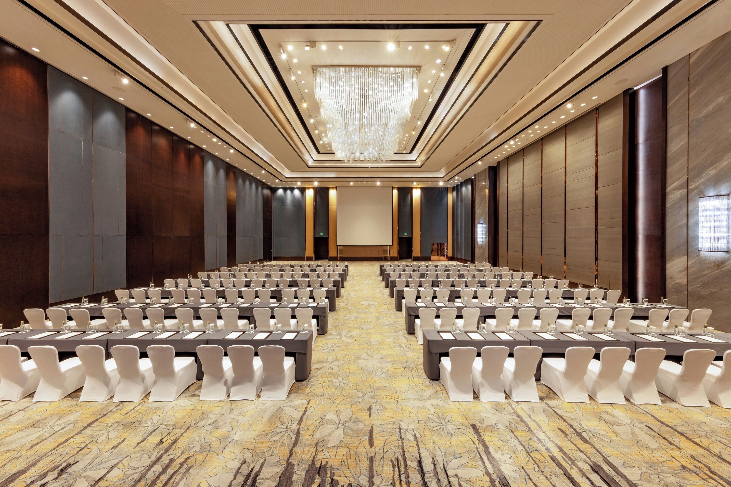 A conference room with rows of tables and chairs, a chandelier, and a patterned carpet.