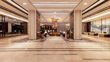 Un vestíbulo espacioso con un mostrador de recepción central, iluminación moderna y un candelabro decorativo.