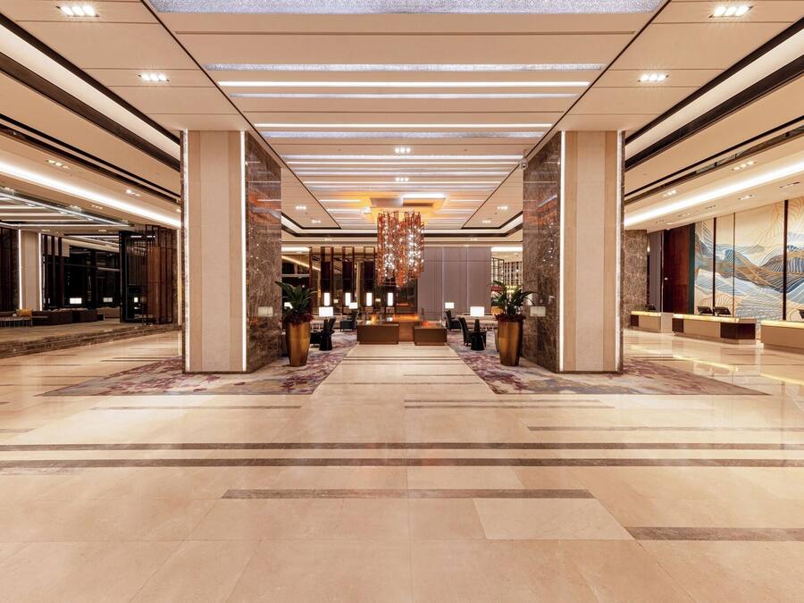 Un vestíbulo espacioso con un mostrador de recepción central, iluminación moderna y un candelabro decorativo.