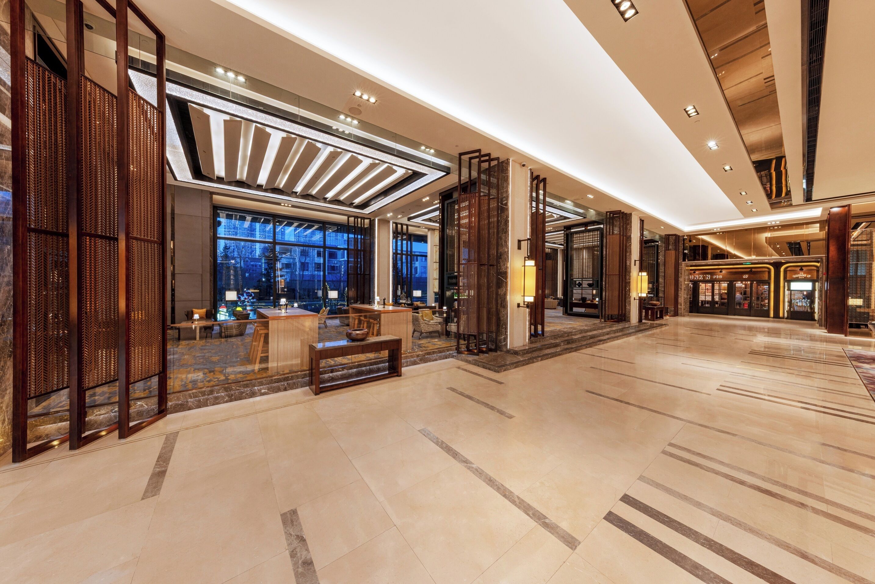 A spacious lobby with a high ceiling, large windows, and a seating area with tables and chairs.