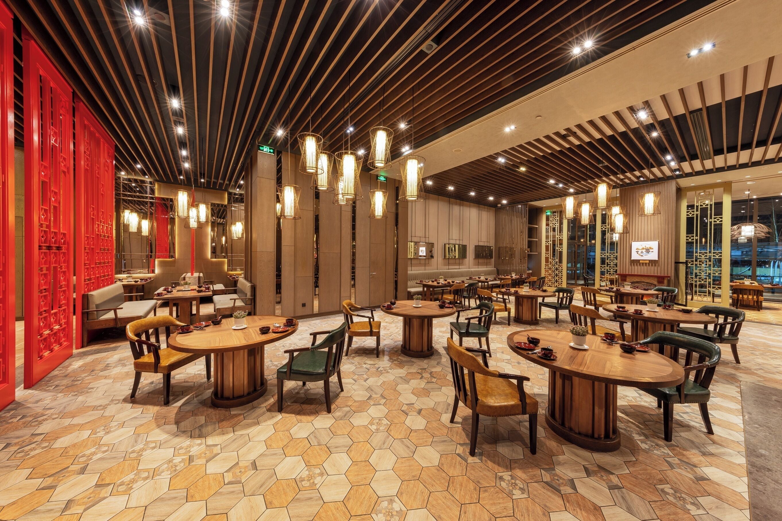 Een ruime restaurantzaal met meerdere ronde tafels en stoelen, een patroon vloer en een modern plafondontwerp.