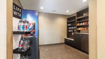 A clean, modern lobby with a life water station, shelves with snacks, and a tiled floor.