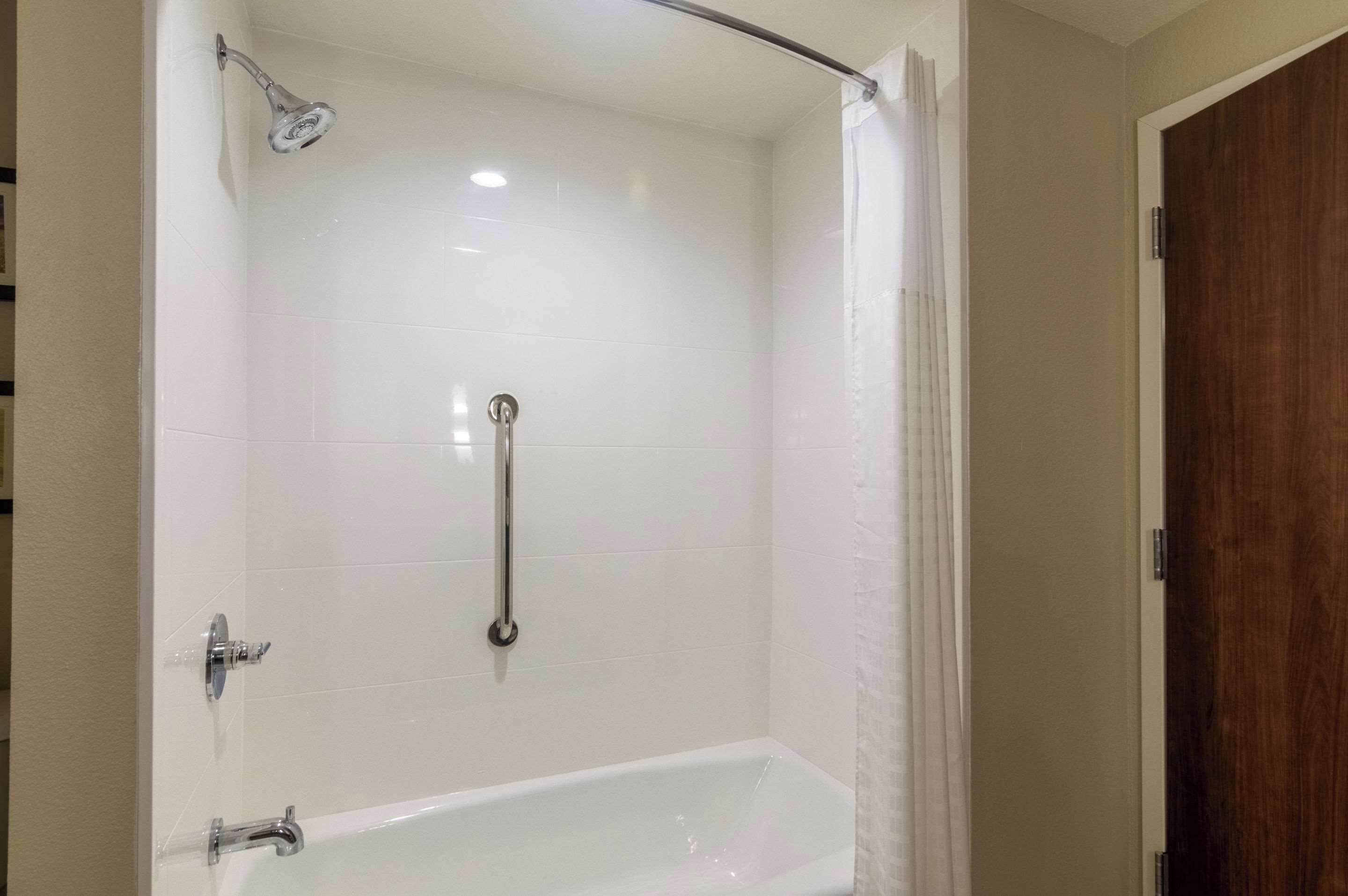 Un baño con una bañera blanca, una ducha con cabezal de ducha de mano y una barra de apoyo.