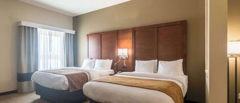 Habitación de hotel con dos camas, un gran cabecero de madera, una ventana con cortinas y una lámpara de noche.