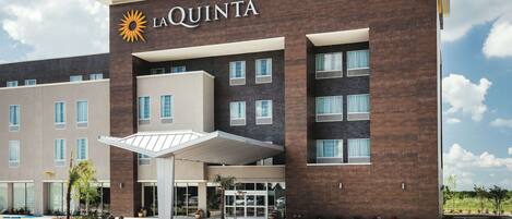 A La Quinta hotel with a modern design, featuring a prominent sun logo, a covered entrance, and a parking lot.