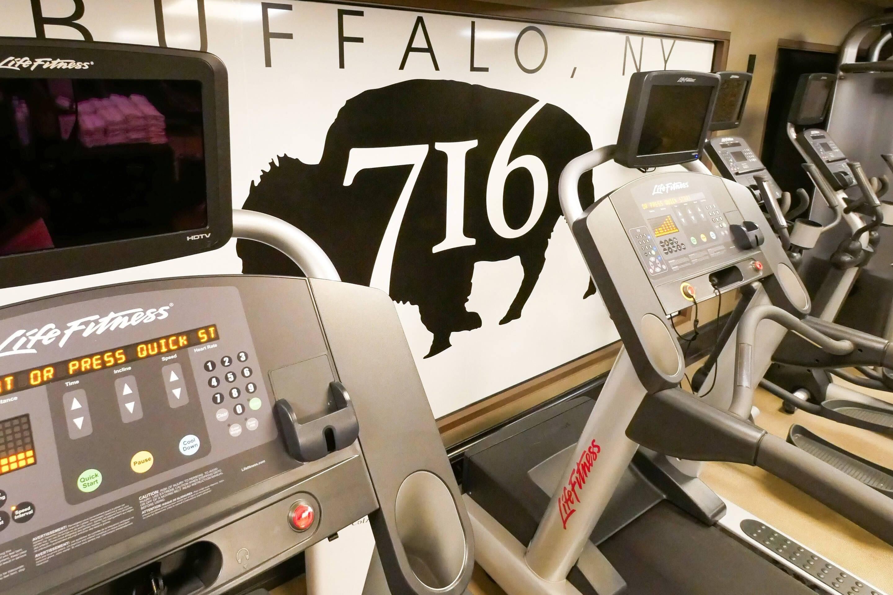 Un gimnasio con cintas de correr, una pantalla digital y un cartel grande con la silueta de un búfalo.